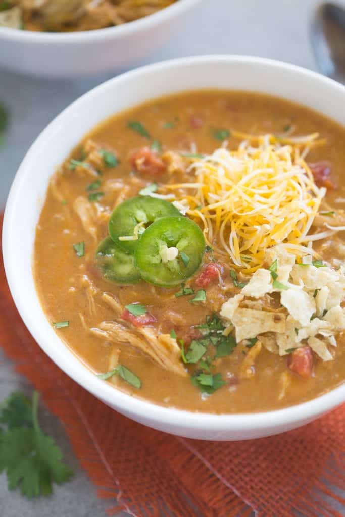 Slow Cooker King Ranch Chicken Soup topped with cheese, tortilla chips, and jalapenos.