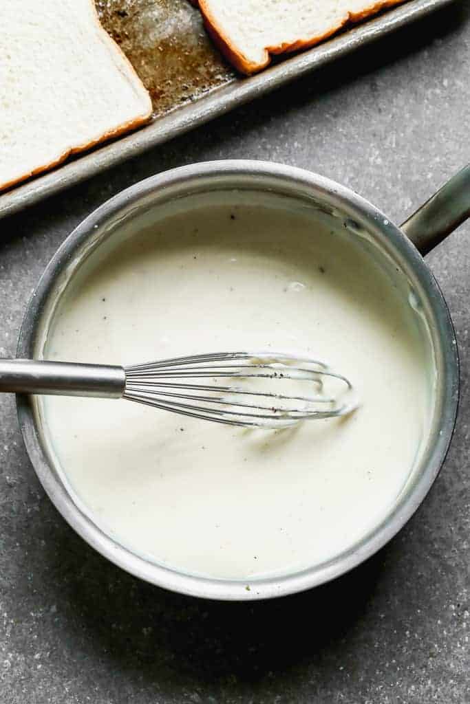 Béchamel sauce cooking in a saucepan with a whisk to stir it.