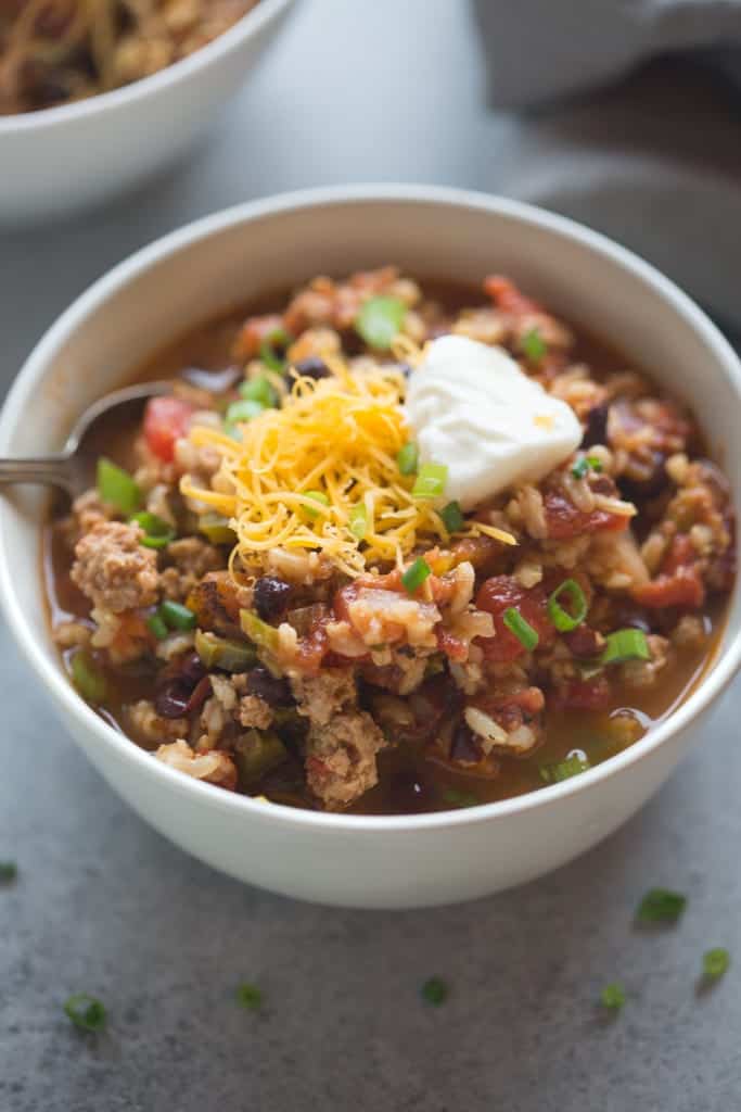 A bowl filled with Spicy Ancho Turkey Chili with shredded cheese and sour cream on top.