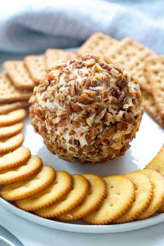 A round plate with a cheese ball (covered in crushed nuts) in the center and crackers fanned in a circle around the edge of the plate.