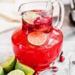 A pitcher of Christmas Punch with fresh cranberries and lime slices floating in it.