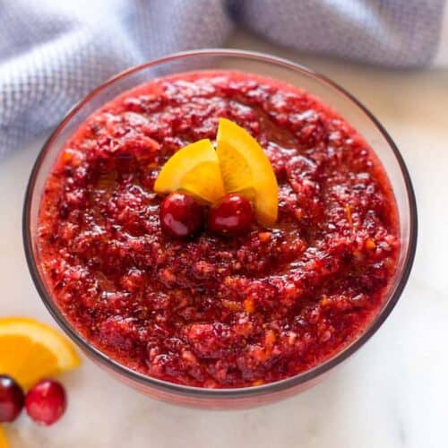 A clear glass bowl of fresh cranberry relish with an orange slice on top.