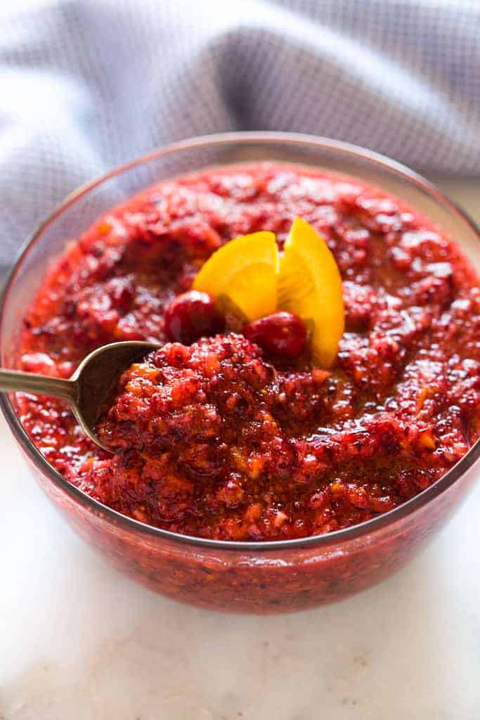 A bowl of cranberry relish with a spoon serving a spoonful.