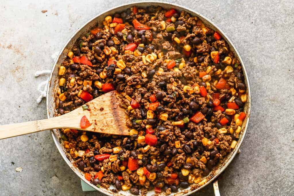 Cook ground beef, black beans, corn and diced bell peppers cooking in a skillet.
