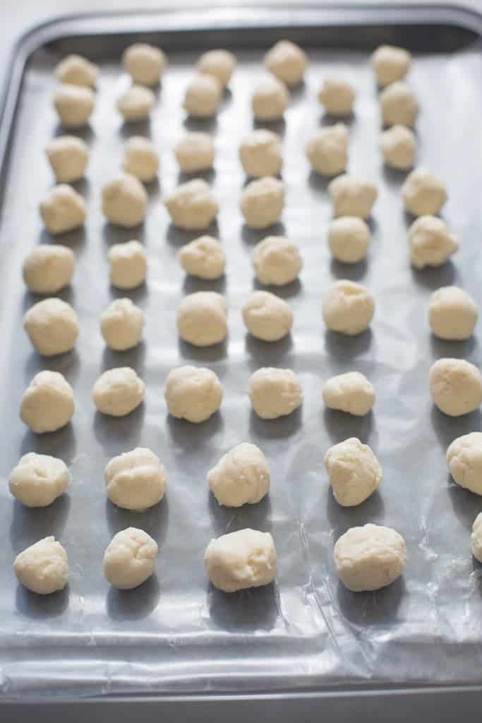 A large baking sheet covered with small vanilla creme balls on parchment paper.