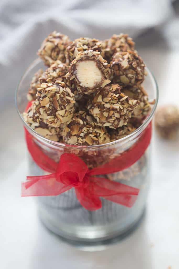 A tall, clear glass with a red bow, filled with vanilla creme balls that have been rolled in crushed nuts.