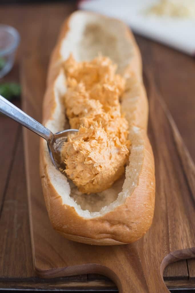 A baguete with the center breading removed and buffalo chicken mixture being spread throughout. 