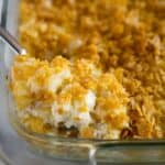A spoonful of funeral potatoes being lifted from a 9x13 inch glass casserole dish.