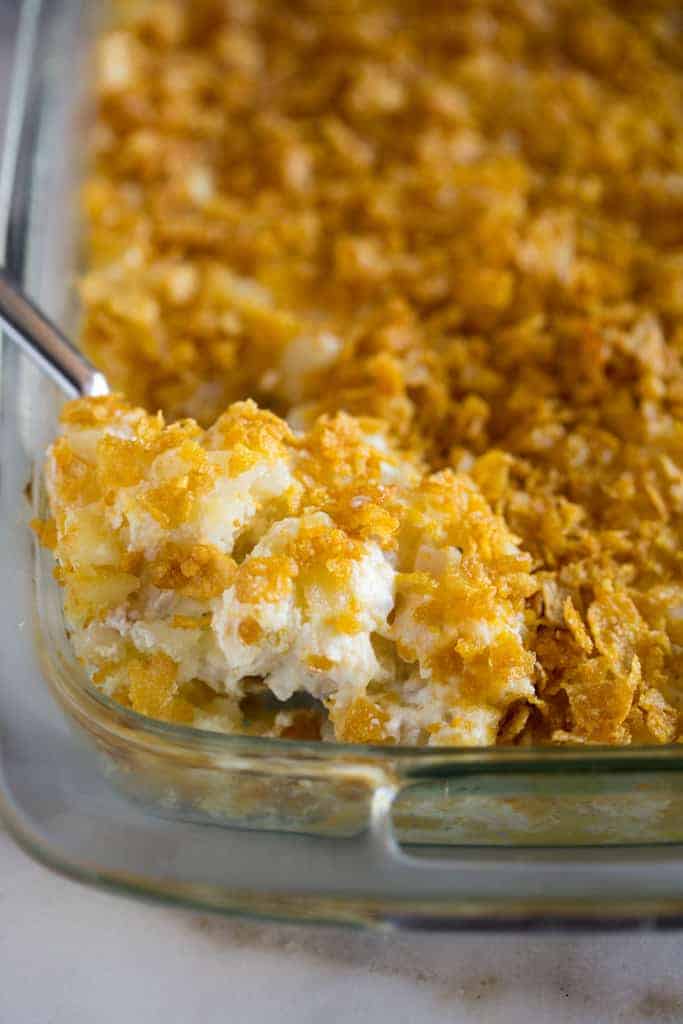 A spoonful of funeral potatoes being lifted from a 9x13 inch glass casserole dish. 