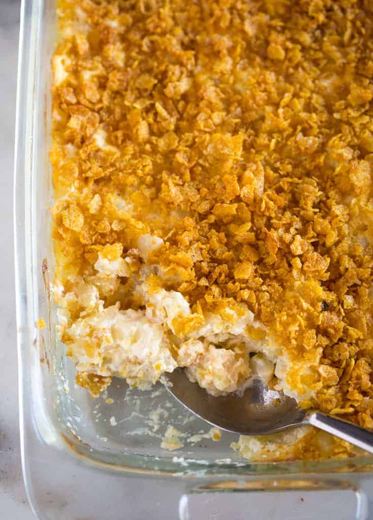 A pan of funeral potatoes with a scoop taken out and a spoon for serving.