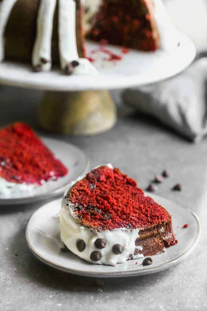 A slice of red velvet cake on a plate, frosted with cream cheese frosting.