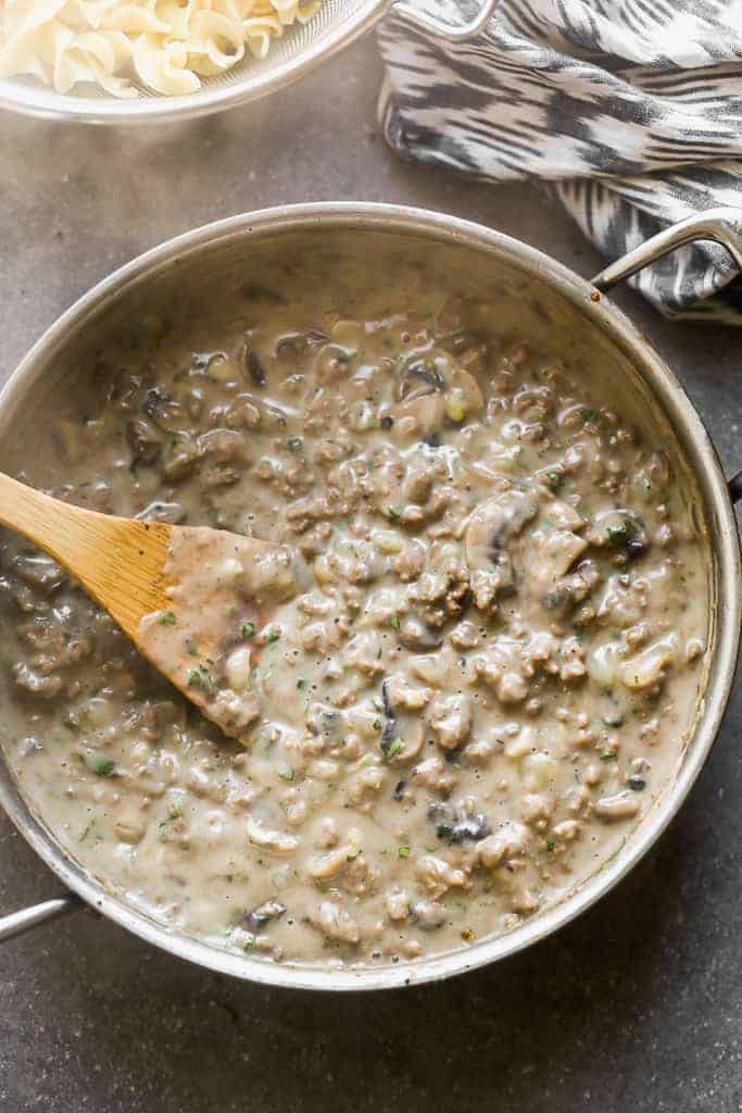 Ground beef stroganoff with mushrooms, in a skillet with a wooden spoon.