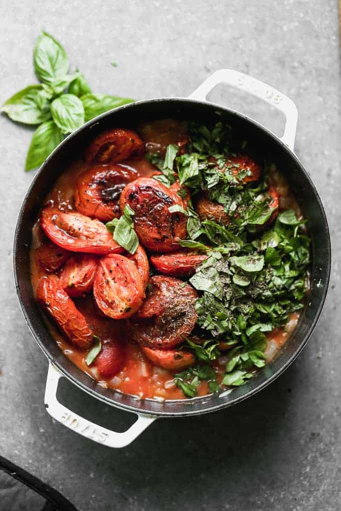 A pot with the ingredients for roasted tomato soup in it, including roasted tomatoes, basil, onion, garlic and broth.