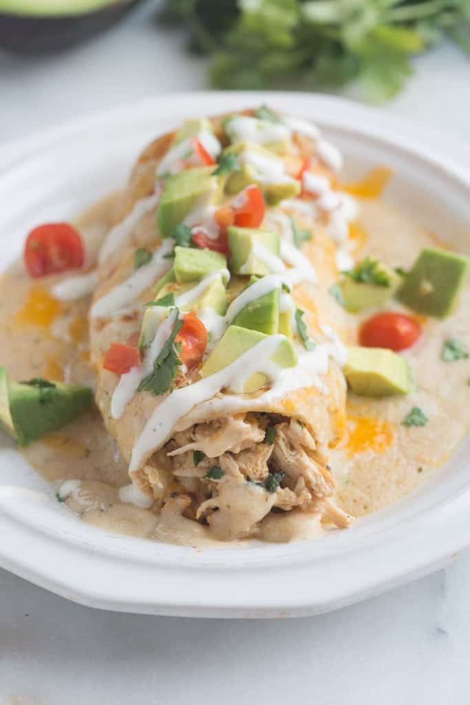 Smothered Ranch Chicken Burritos with avocado and tomatoes on top on a white plate.