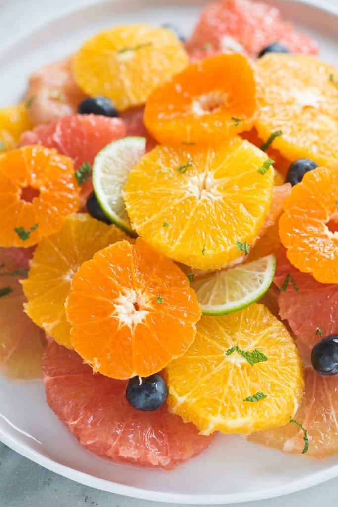 Citrus Fruit Salad ring slices of grapefruit, pomelo, tangerine, clementines, and blueberries on a white plate.