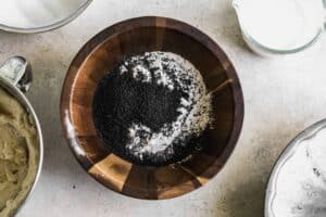 A wooden mixing bowl with flour, salt, baking powder and poppyseeds.