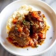 Two braised short ribs and mashed potatoes on a white plate.