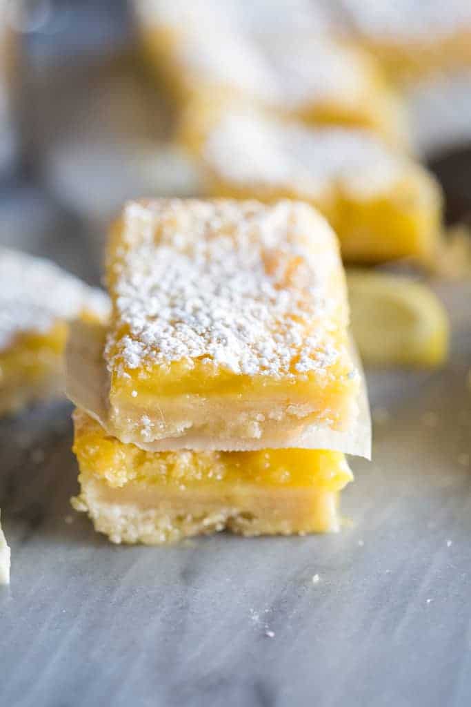 A stack of two lemon bars with powdered sugar on top and more lemon bars in the background.