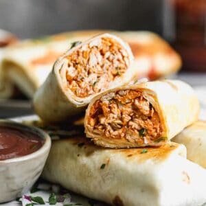 A BBQ chicken wrap cut in half to show the filling inside the tortilla, stacked with other wraps on a plate.