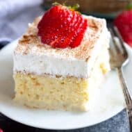 A slice of Tres Leches Cake with a sliced strawberry on top, served on a plate.