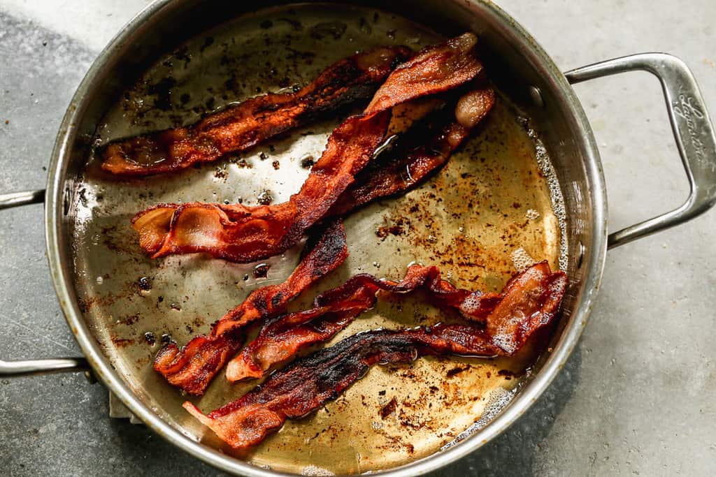 Slices of bacon cooking in a pot.