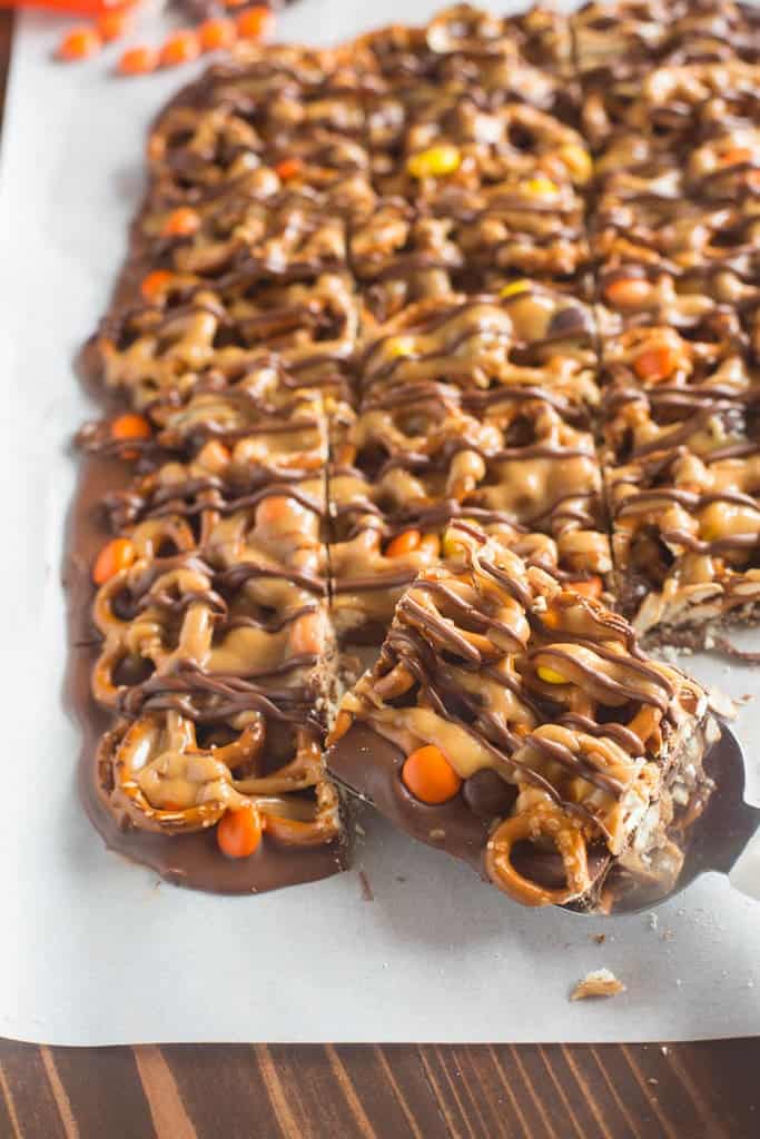 Melted chocolate topped with pretzels, Reese's pieces, and a simple peanut butter sauce on wax paper.
