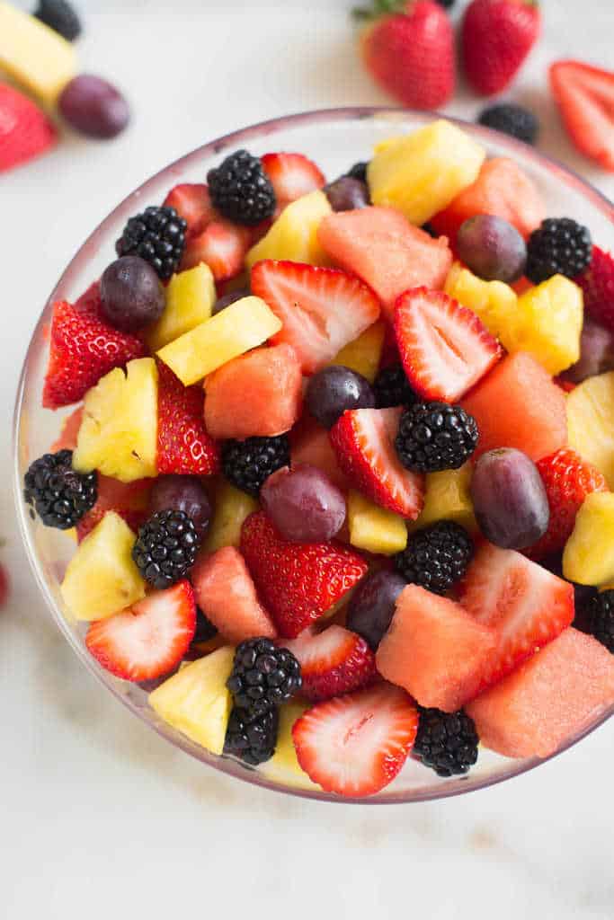 Strawberries, pineapple, blackberries, grapes, and watermelon in a large glass bowl.