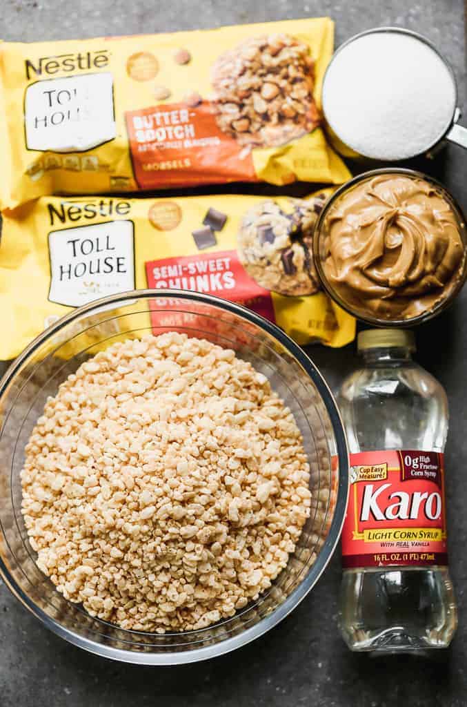 The ingredients needed for scotcheroos including rice krispies in a bowl, karo syrup, peanut butter, sugar, chocolate chips and butterscotch chips.