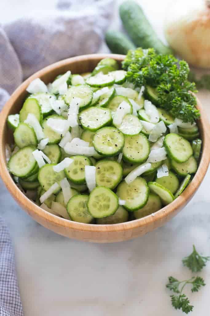 A wooden bowl filled with sliced english cucumbers and onions.