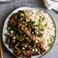 Mongolian beef on a plate with rice and chopped green onion on top.