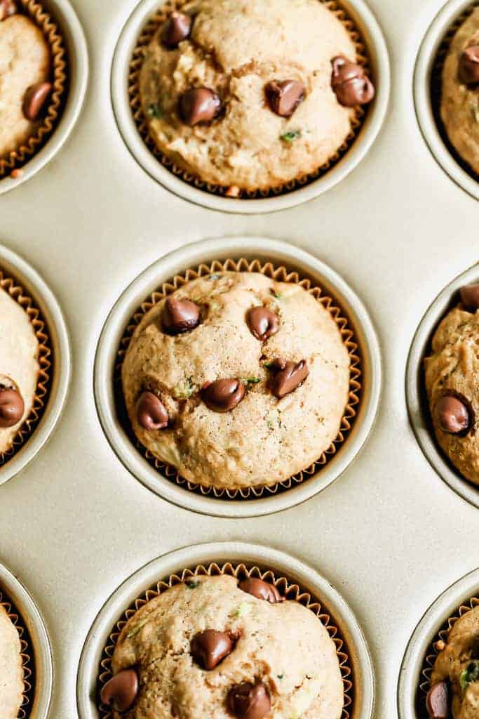 A muffin tin with baked zucchini muffins in it.