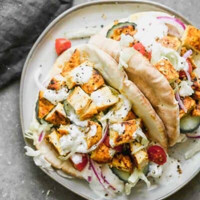 A plate with two chicken gyros in pitas, with tzatziki, onion, cucumber and tomato.