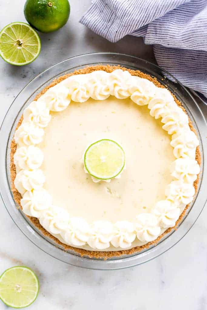 A whole key lime pie with piped whipped cream around the edges and a lime wedge in the center.