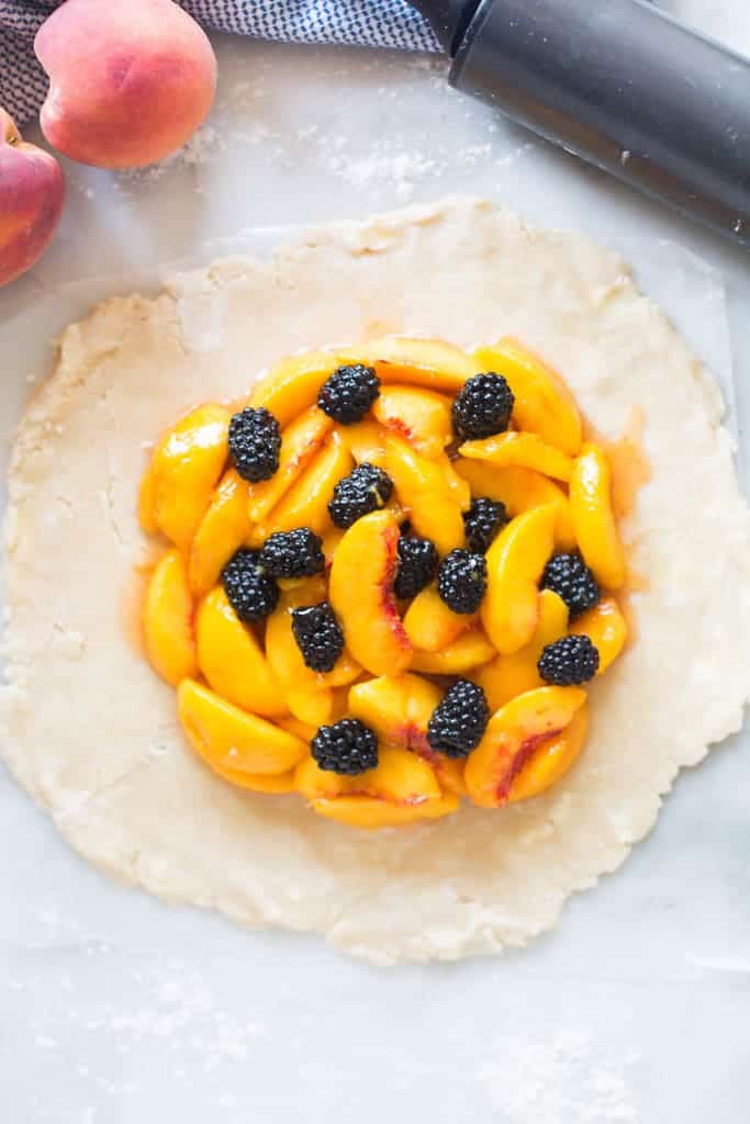 Pie crust that has been rolled out and is topped with fresh peaches and blackberries for a tart.