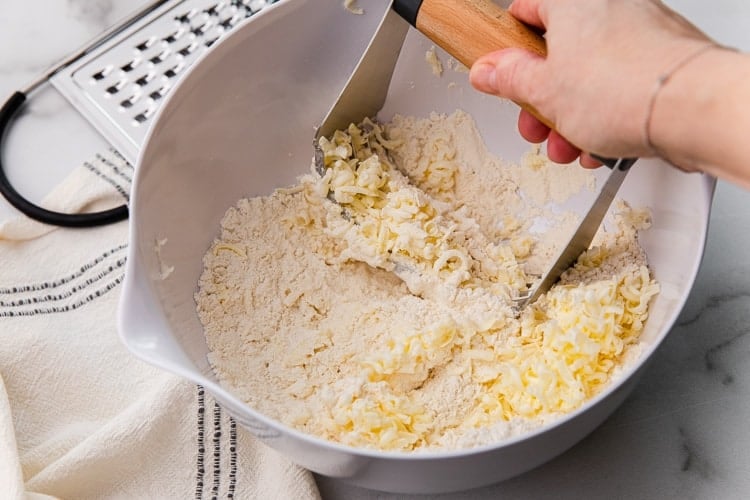 Cold butter being cut into flour mixture with a pastry blender.