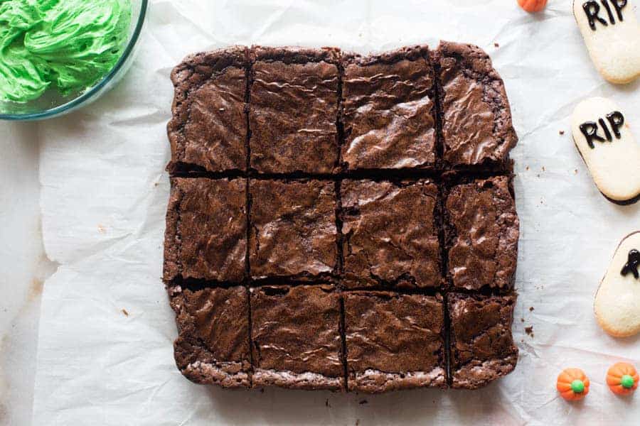 Baked brownies laying on parchment paper and cut into 12 rectangles.