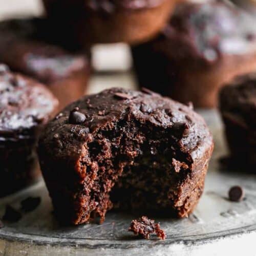 Healthy Chocolate Muffins stacked on a plate with a bite taken out of one.