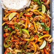 A sheet pan with cooked chicken and bell peppers seasoned for fajitas.