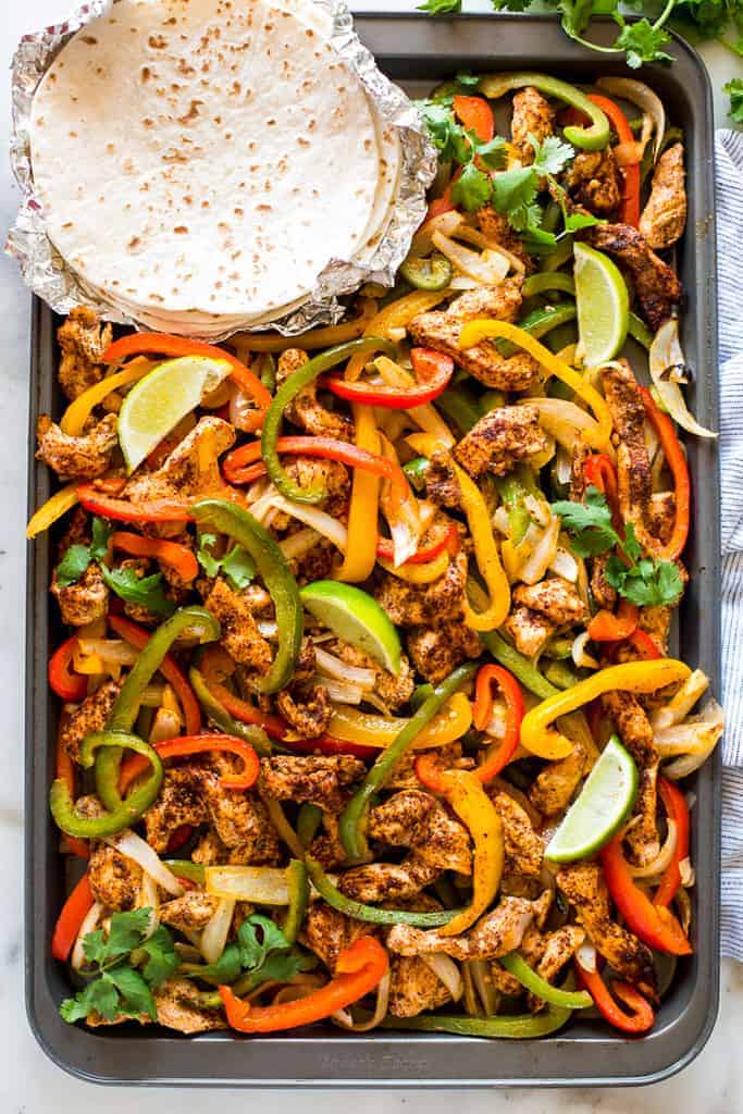 A sheet pan with cooked chicken and bell peppers seasoned for fajitas.