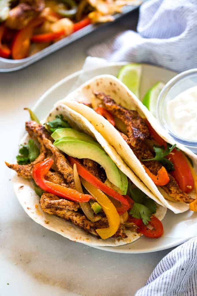 A plate with two chicken fajitas inside tortillas and sour cream on the side.