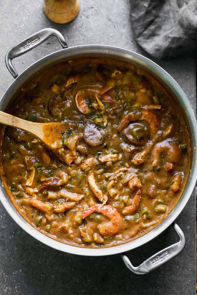 A stockpot full of gumbo with chicken, sausage and shrimp in it and a wooden spoon.