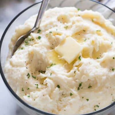 A bowl of creamy mashed potatoes with a slice of butter, and a large serving spoon.
