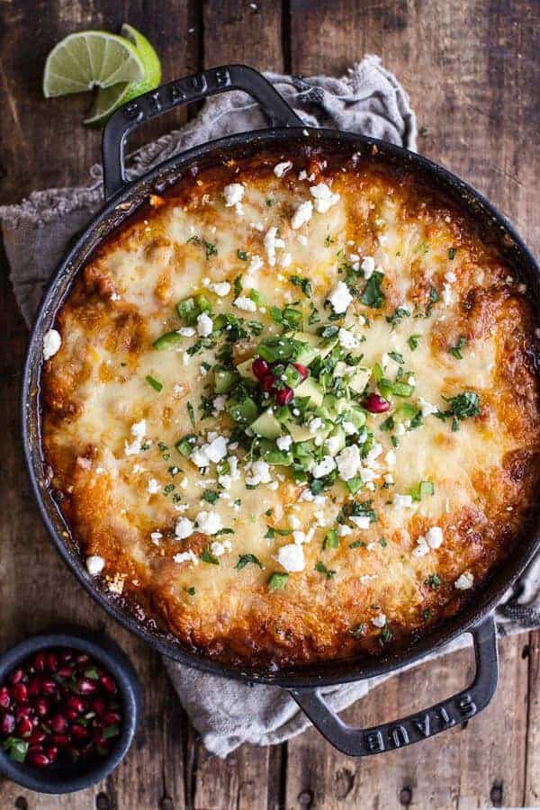 A cast iron skillet with containing cheesy turkey tamale pie and topped with cilantro, avocado and feta on a wood background.  
