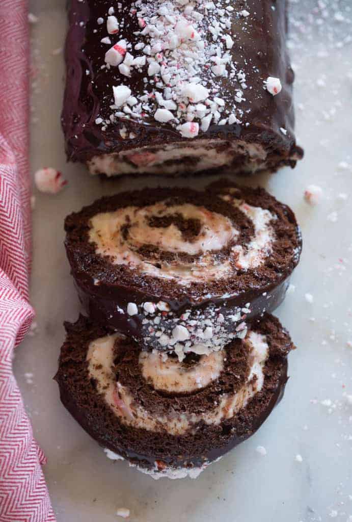 Overhead view of a Chocolate Peppermint Cake Roll with two slices overlapping each other, next to a red dish towel.