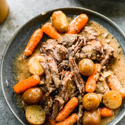 Cooked pot roast with baby potatoes and carrots and gravy on top.