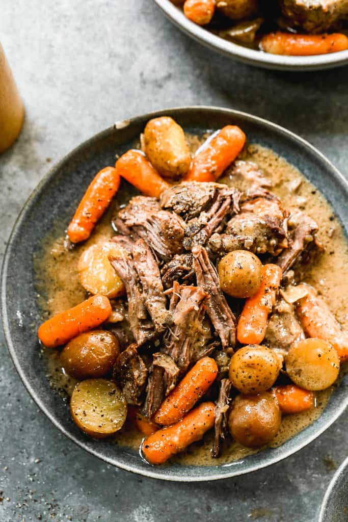 Cooked pot roast with baby potatoes and carrots and gravy on top.