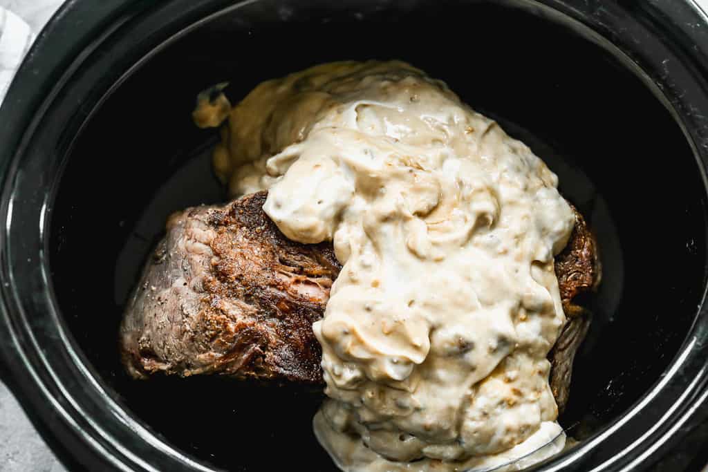 Seared pot roast in a pot with sauce poured on top.