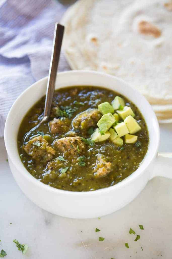 Authentic chile verde pork garnished with fresh avocado and served with a side of flour tortillas. - tastesbetterfromscratch.com