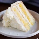 A slice of Coconut Cake with pineapple filling, laying on a white plate.