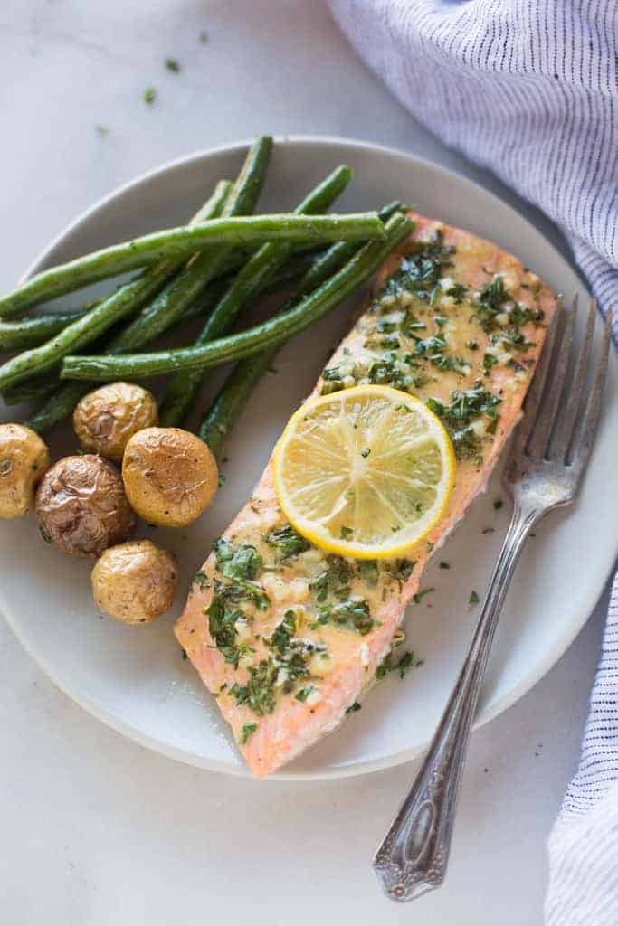 A salmon filet topped with lemon dijon sauce, on a plate with a side of green beans and potatoes.